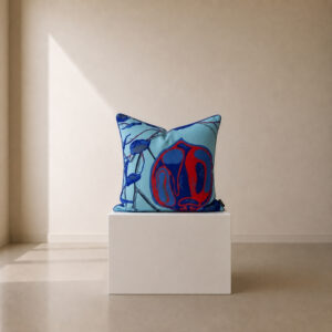 Decorative scatter cushion featuring an abstract botanical-inspired illustration in vibrant red and deep blue on a soft aqua background, displayed on a minimalist white plinth.
