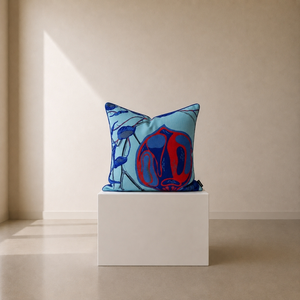 Decorative scatter cushion featuring an abstract botanical-inspired illustration in vibrant red and deep blue on a soft aqua background, displayed on a minimalist white plinth.